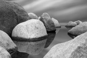 Black and white photography of floating stones on water by iCanvas artist Jeff Friesen