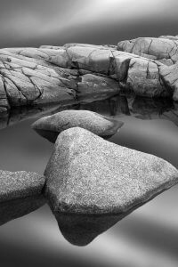 Black and white photography of floating stones on water by iCanvas artist Jeff Friesen