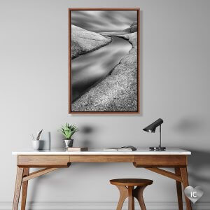 Framed black and white photo of a stream going between stones by iCanvas artist Jeff Friesen mounted above a desk